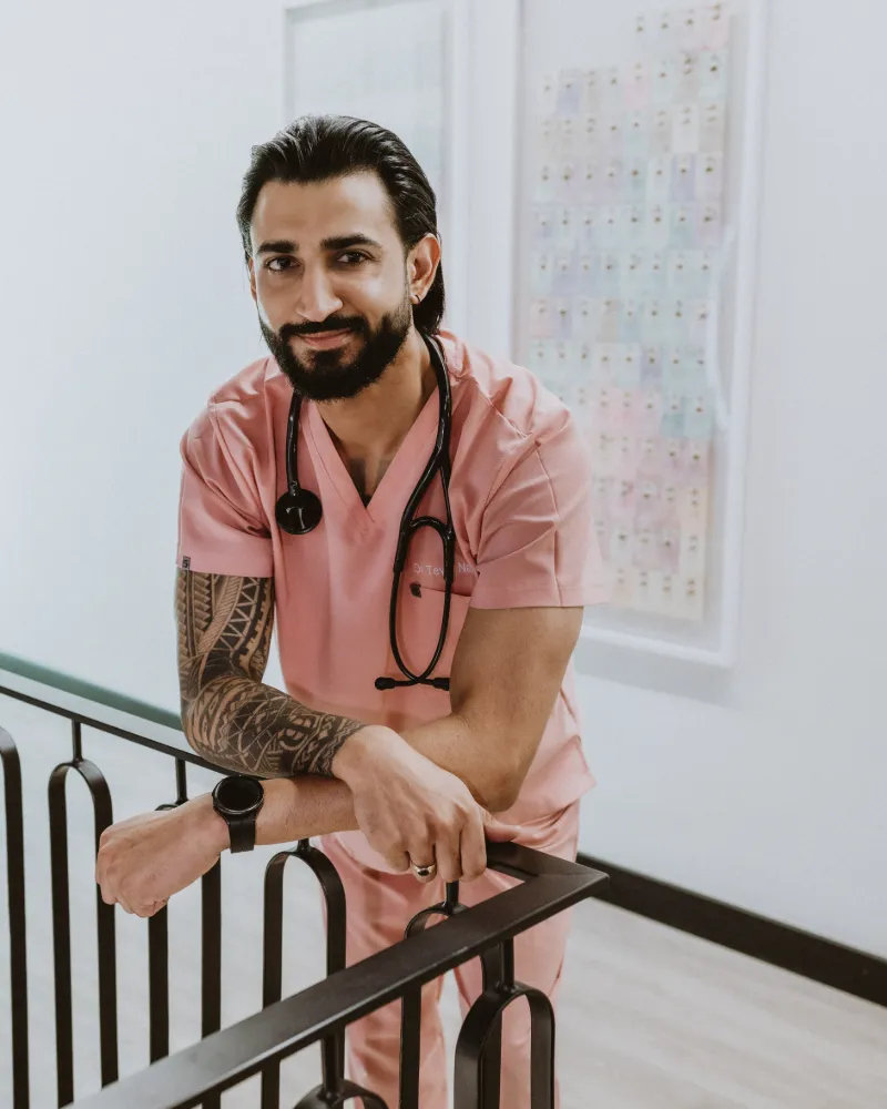 Dr Tevin Naidu in pink scrubs with a stethoscope, smiling as he leans on a stair railing
