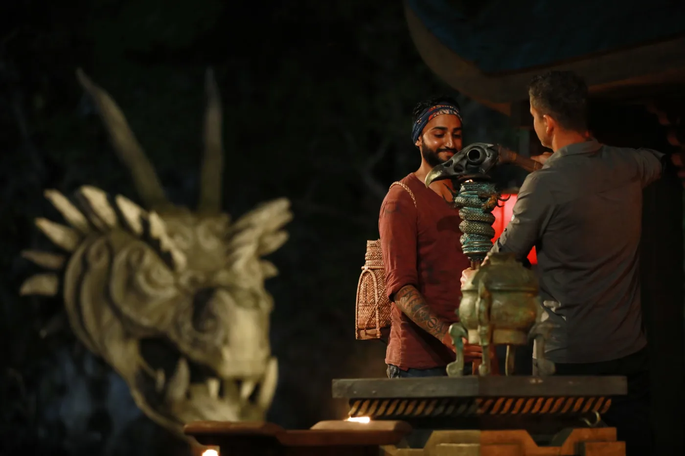 Dr Tevin Naidu in a blue buff smiling at Tribal Council as host Nico Panagio snuffs a torch, Survivor South Africa: Philippines